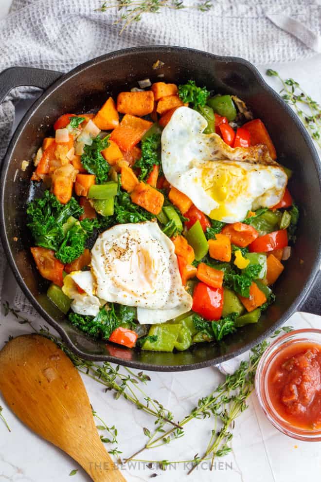 fried eggs over easy in a cast iron skillet surrounded with colorful vegetables