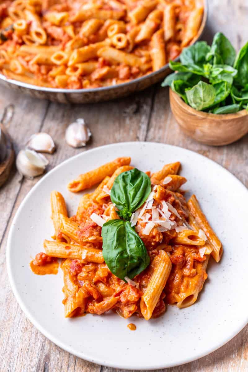 vodka sauce with pene on a plate next to a pan of vodka pene pasta