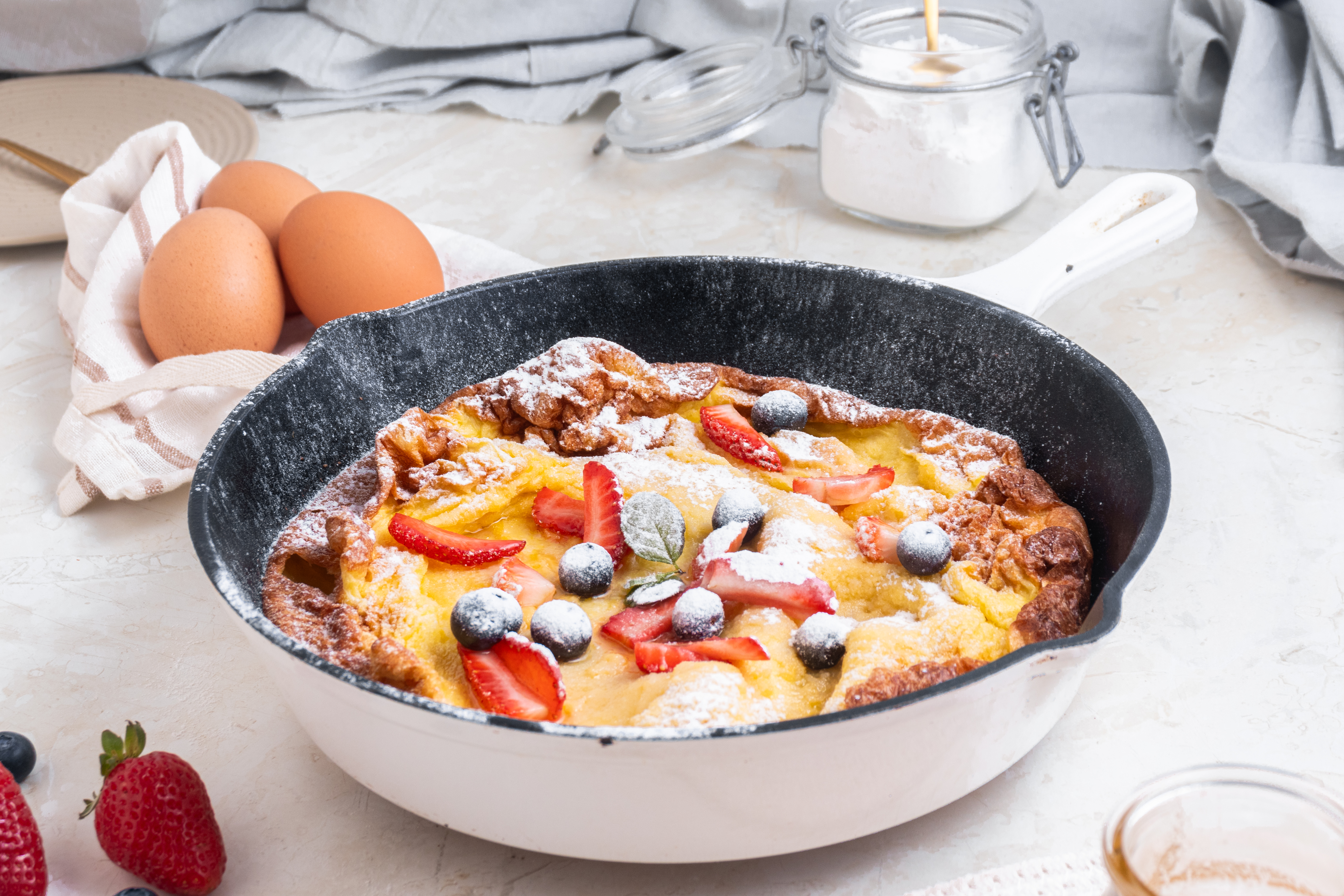 dutch baby pancake in a cast iron skillet with powdered sugar and fruit