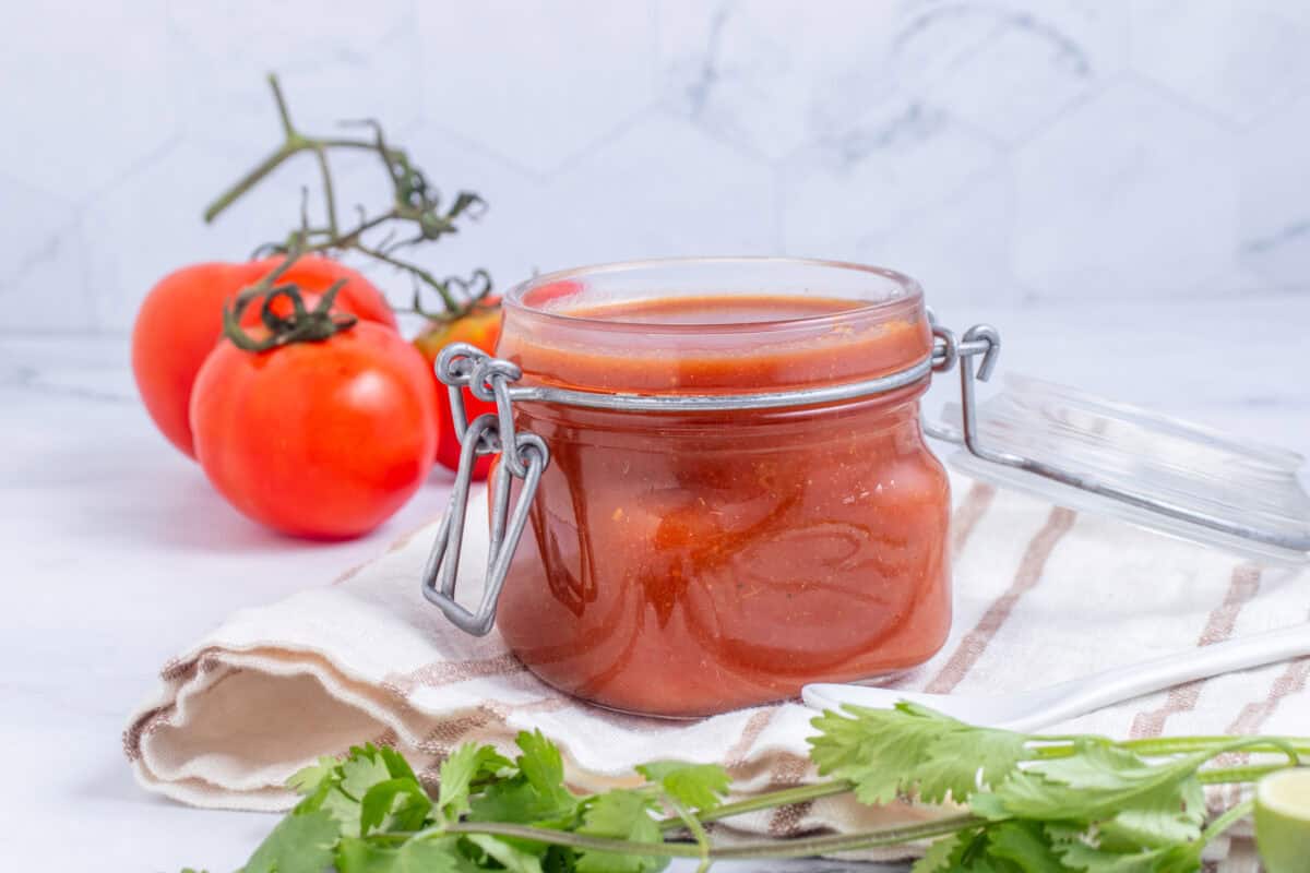 taco sauce in a jar next to a tomato and fresh cilantro