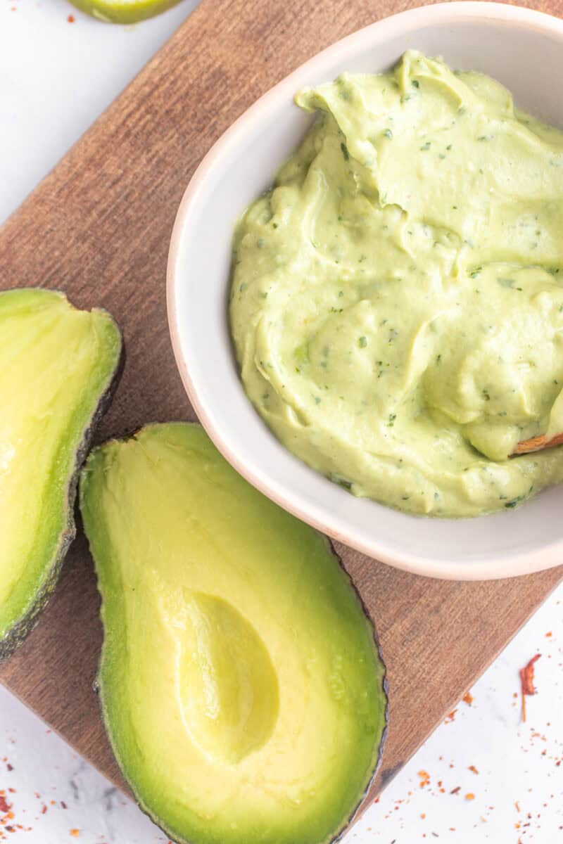 avocado crema in a bowl next to two avocado halves